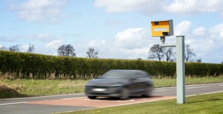 Car speeding past a yellow roadside speed camera on a UK road