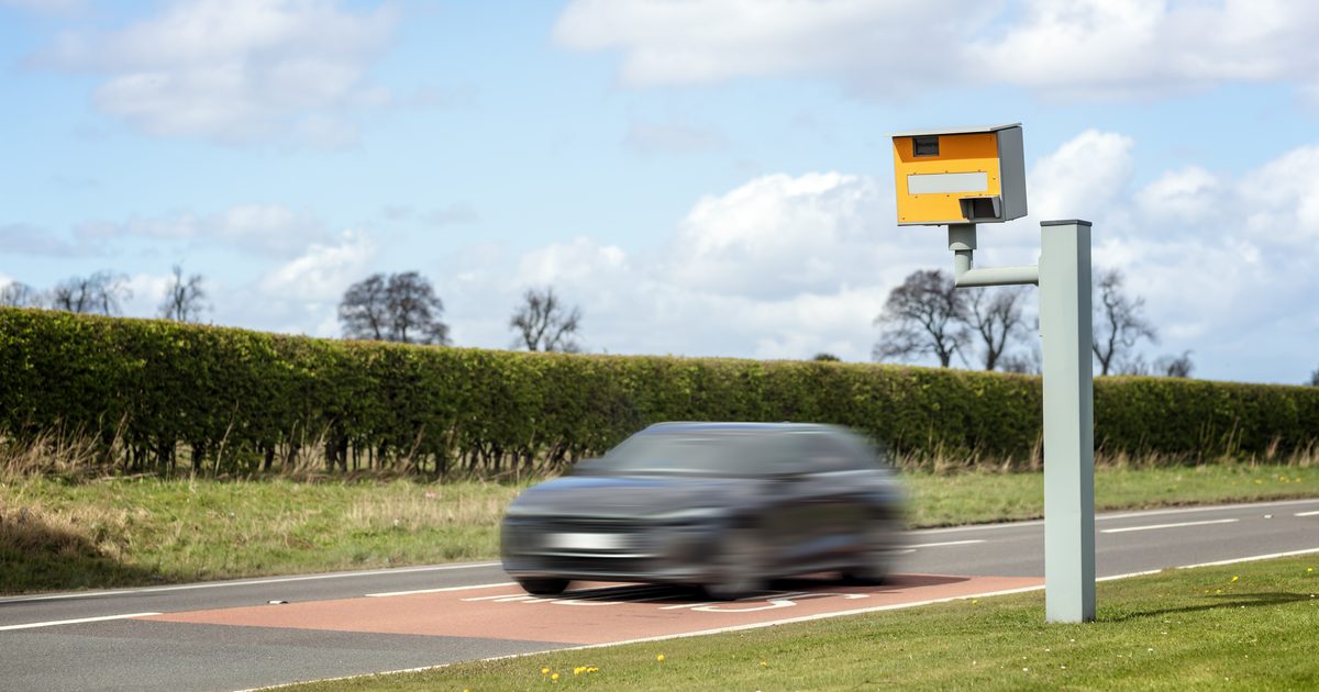 Car speeding past a yellow roadside speed camera on a UK road